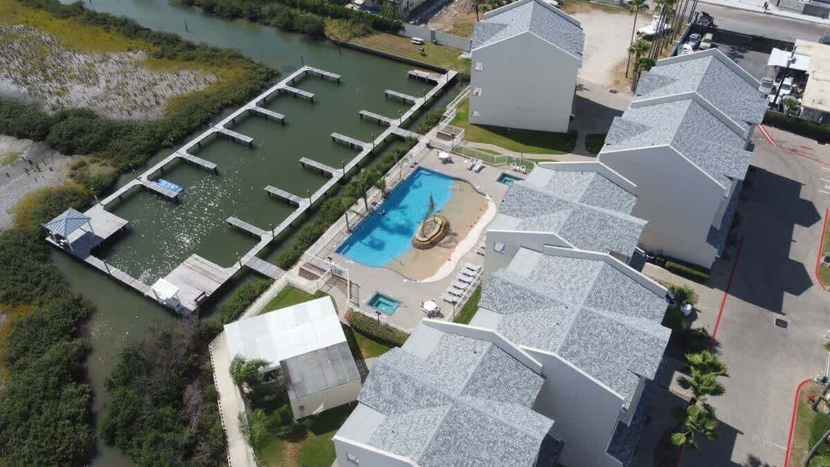 An aerial view of a residential area with a swimming pool, docked boats, and modern houses.