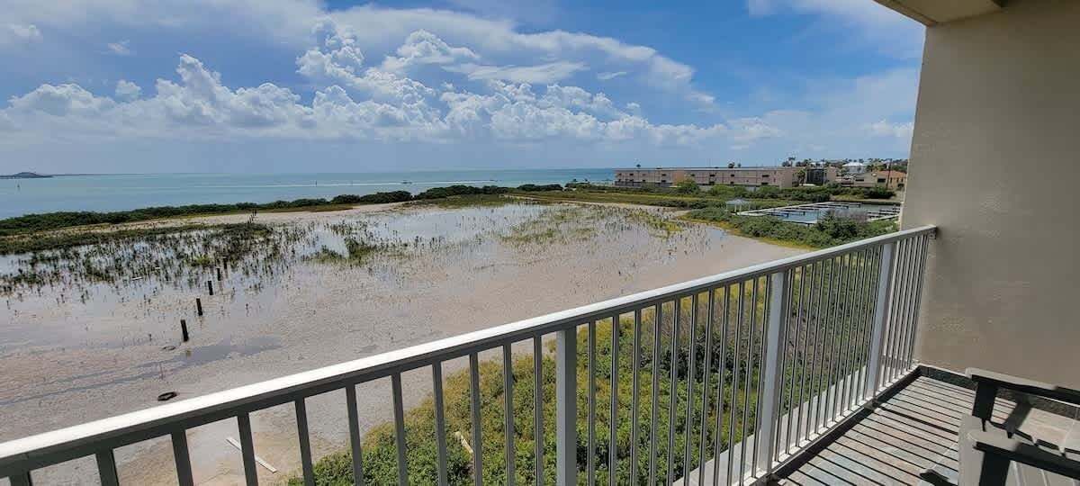A balcony with a view of a beach and a distant building.