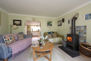 A cozy living room with a fireplace, a sofa, a coffee table, and a dining table. - A cosy cottage with a woodburner (Gwithian)