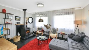 Ein modernes Wohnzimmer mit Kamin in Schwarz, zwei Sesseln, einem grauen Sofa, einem roten Teppich und einem Bücherregal.