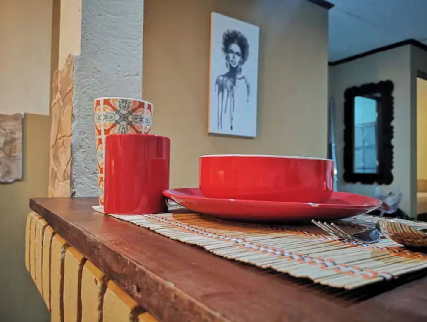 Un coin repas avec une table en bois, de la vaisselle rouge et un set de table à motifs.