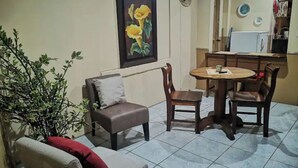 A living room with a sofa, a small table, and a chair. There is a painting on the wall and a plant on the floor. - Casa Central Playa Jacó Downtown A Pocos Pasos de la Playa (Jacó)