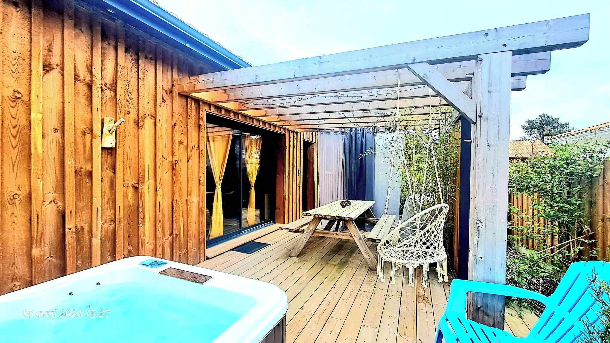Une terrasse en bois avec un jacuzzi, une table, des chaises et une structure en forme de pergola.