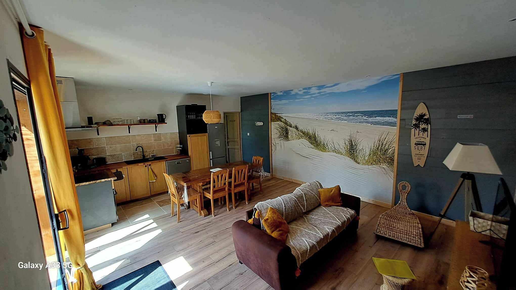 A compact living space with a kitchen, dining area, and a large beach mural.