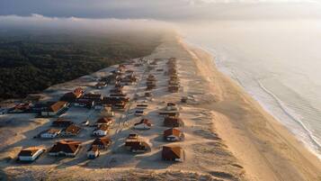 Luchtbeeld van een kustdorpje met huizen langs het strand, omgeven door beboste heuvels.