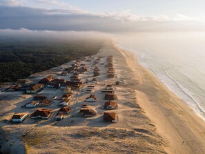 Vista aerea di un villaggio costiero con case allineate lungo la spiaggia, circondato da colline boscose.