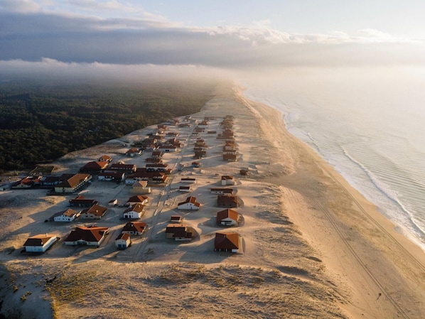 An aerial view of a coastal village with houses aligned along the beach, surrounded by forested hills. - Les Bord'Océanes Villa Marensine and Villa Oyat – Private Sauna & Spa (Vielle-Saint-Girons)