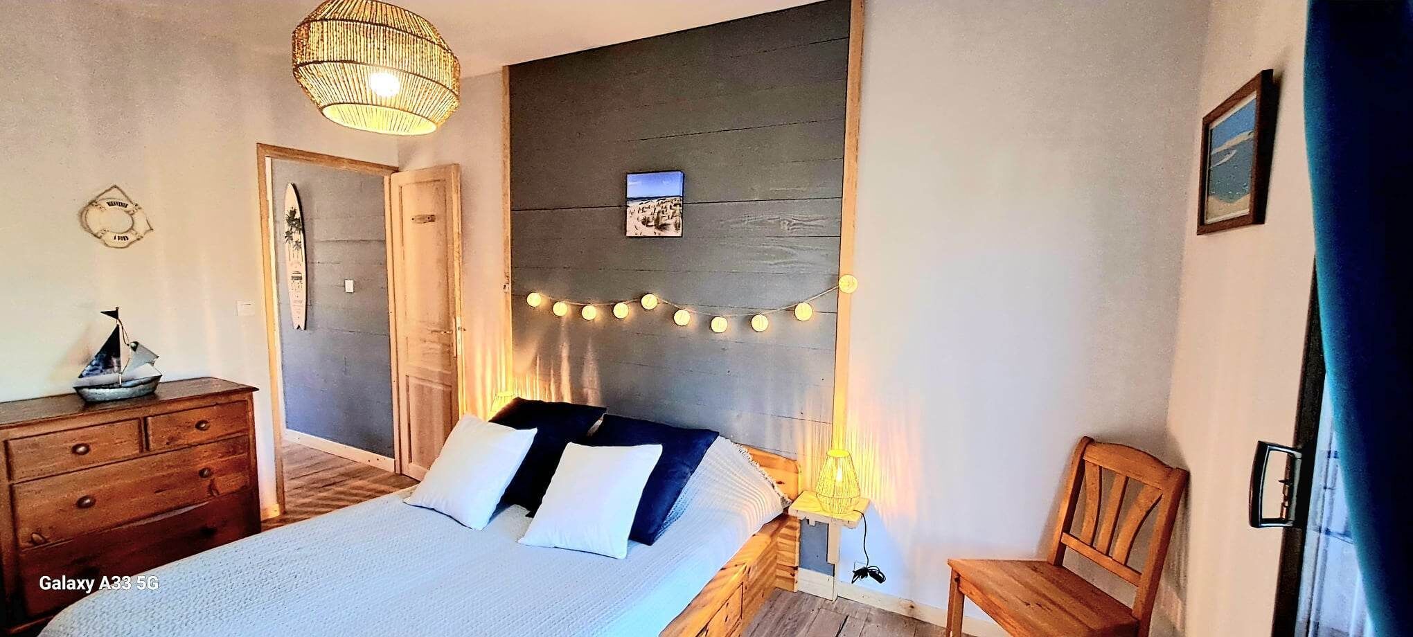 Een slaapkamer met een bed, een houten dressoir, een stoel, een wandplank en een lichtslingering.