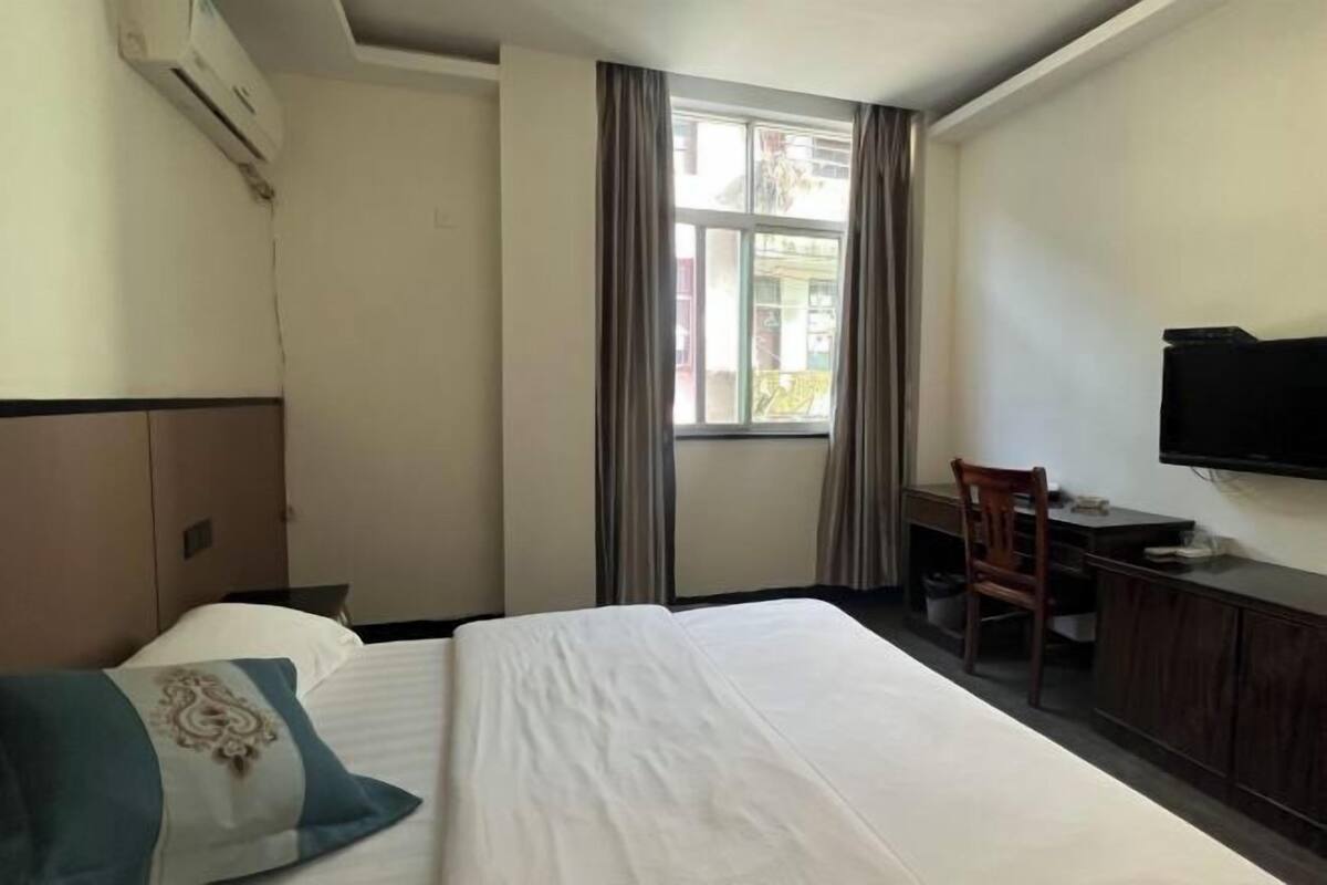 A hotel room with a bed, a desk, a chair, a TV, and a window with curtains.