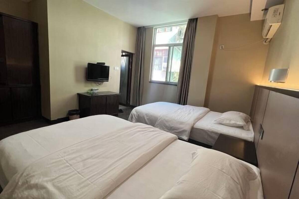 A hotel room with two beds, a television, a wardrobe, and a window with curtains.