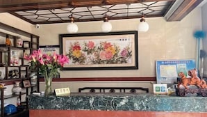 Zona de recepció amb un taulell de marbre, obra d'art floral emmarcada i un ram de flors roses.