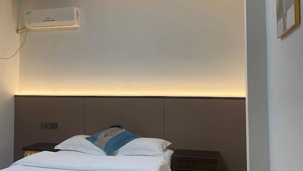 Habitació d'hotel amb llit, taula de nit i unitat de climatització penjada a la paret.