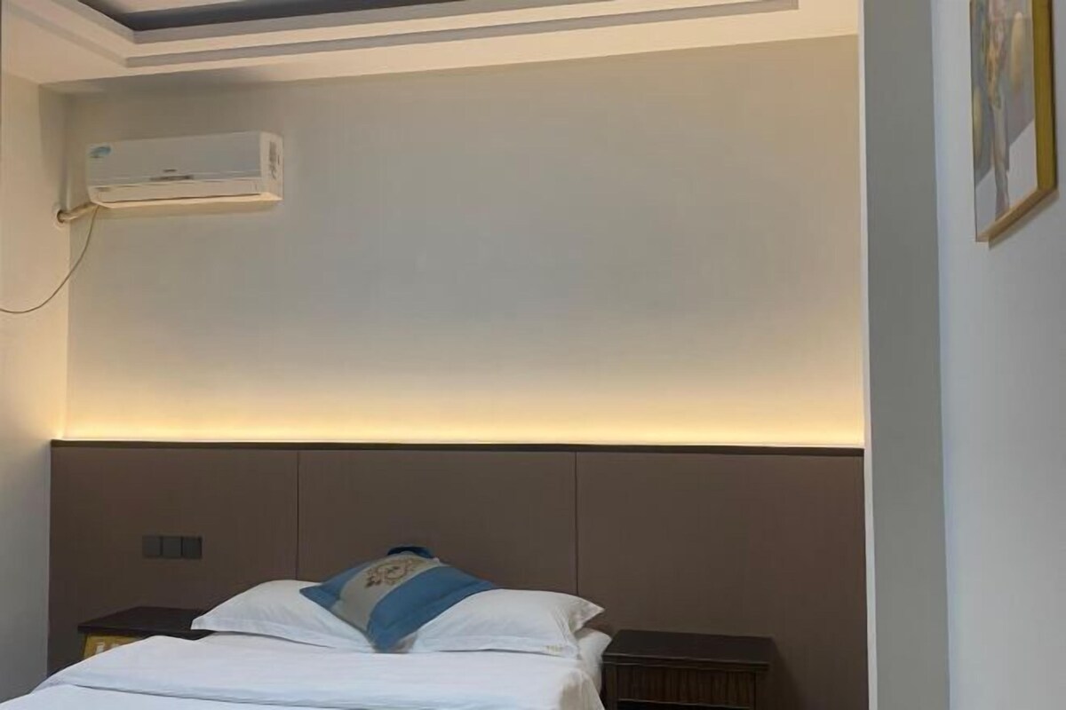 A hotel room with a bed, bedside table, and an air conditioning unit mounted on the wall.
