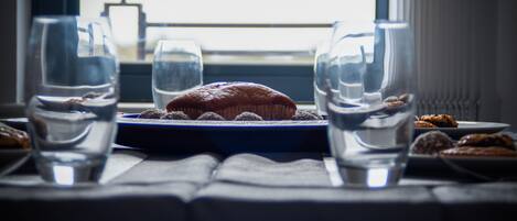 A table with a muffin on a plate, surrounded by clear glasses of water, set by a window with a view.