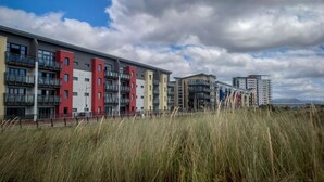 Une rangée d’immeubles modernes à plusieurs étages, dotés de balcons, se dressant sur fond d’un ciel partiellement nuageux.
