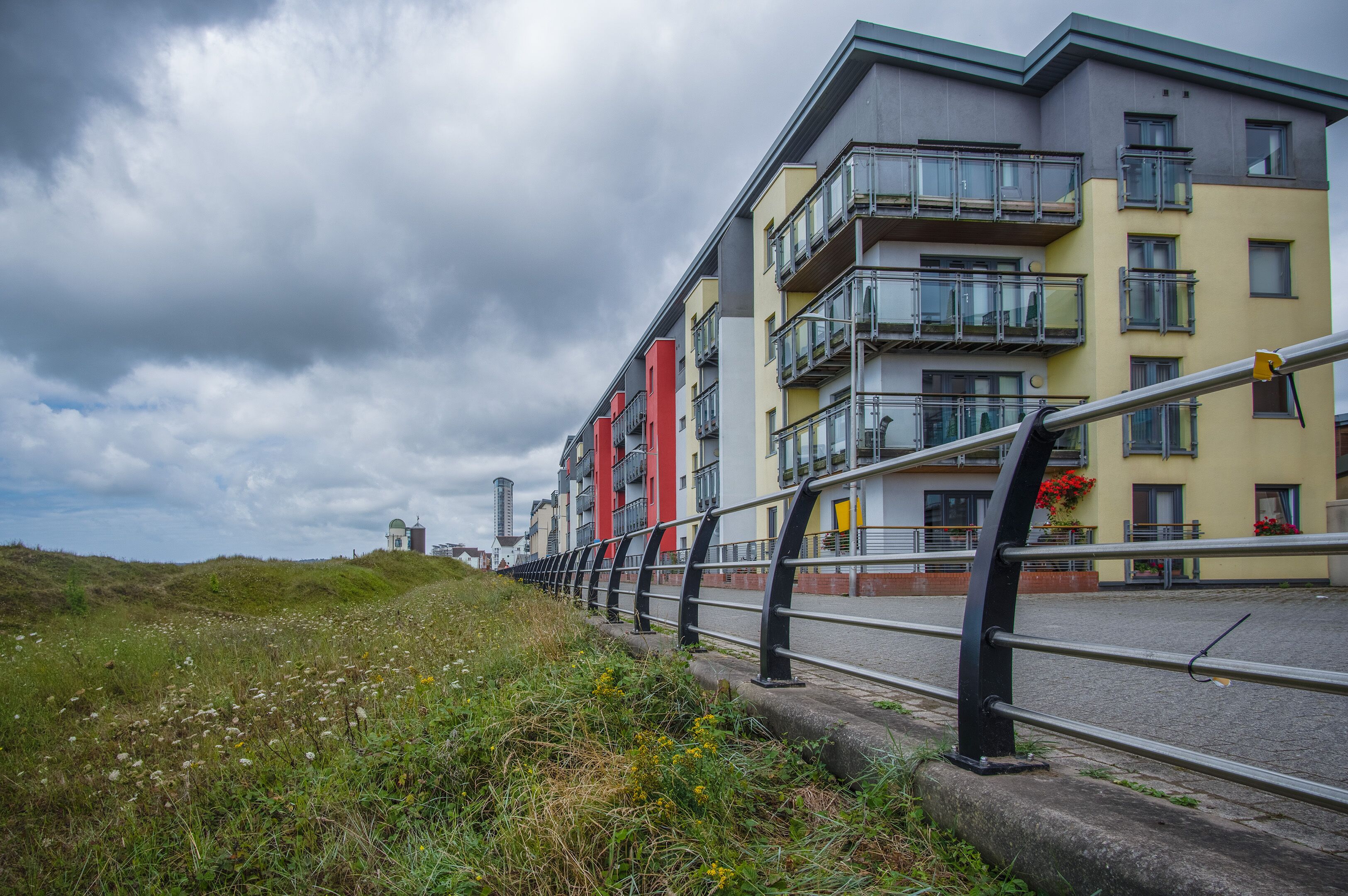A modern apartment building with balconies, a paved pathway, and a grassy area.