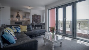 Un salon moderne avec un canapé en cuir noir, une table basse en verre et une vue sur le balcon.