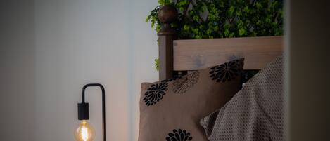 Una cama bien hecha con almohadones estampados y una lámpara de pared.