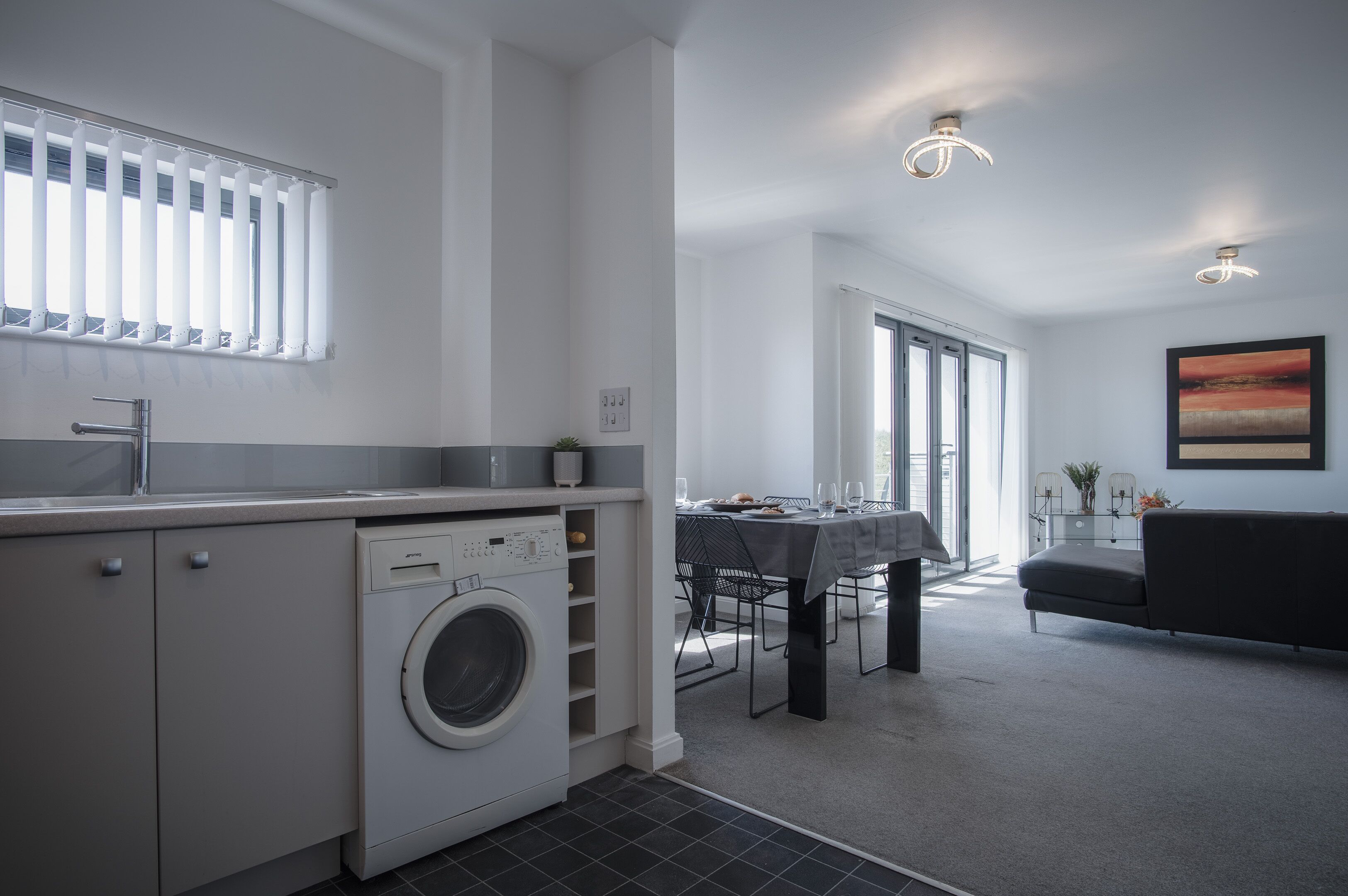 A modern kitchen with a built-in washing machine, a dining area with a table and chairs, and a living area with a sofa.