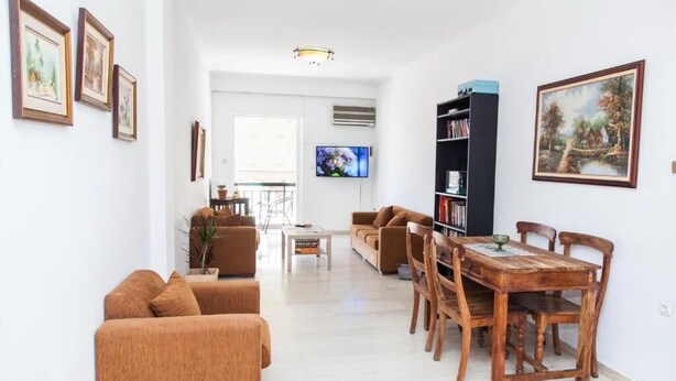 A living room with a sofa set, a dining table with chairs, a TV, and a bookshelf. - Fabulous Apartment in Pireaus (Piraeus)