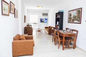 A living room with a sofa set, a dining table with chairs, a TV, and a bookshelf. - Fabulous Apartment in Pireaus (Piraeus)