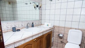 A bathroom with a white sink, wooden cabinets, a mirror, a toilet, and a shower area. - Fabulous Apartment in Pireaus (Piraeus)
