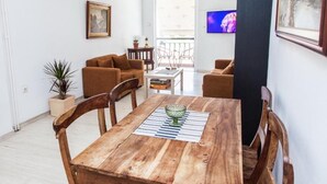 A living room with a wooden dining table, two sofas, a TV, and a balcony with a view. - Fabulous Apartment in Pireaus (Piraeus)