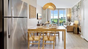 A modern kitchen with a stainless steel refrigerator, a dining table with chairs, a hanging light fixture, and a view of the outdoors through large windows. - Modern Resort : Balcony+ Gym+ Amazing Pool (Hallandale Beach)