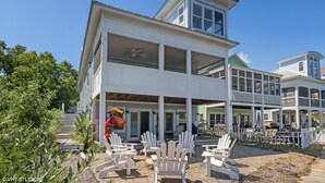 A large, multi-story house with a covered patio area featuring white Adirondack chairs and a dining table.