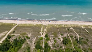 An aerial view of a beach with a sandy shore, a clear blue ocean, and a forested area with paths.