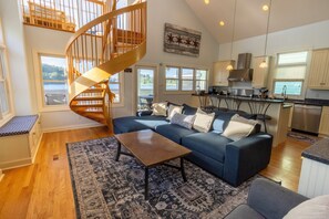 A modern living room with a spiral staircase, a blue sofa, and a view of the lake. - Beach House on Lake Kai in Beachwalk Resort (Michigan City)
