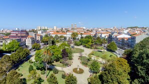 A cityscape with a mix of modern and historic buildings, a central park with a statue, and a clear blue sky. - Select Porto (Porto)