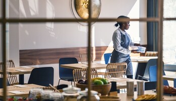 A restaurant interior with tables, chairs, and a waiter.