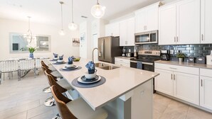 A modern kitchen with white cabinets, stainless steel appliances, and a central island with blue napkins. - Last Minute Disney Getaway! Townhouse with Private Pool. Book Now! #21174 (Orlando)