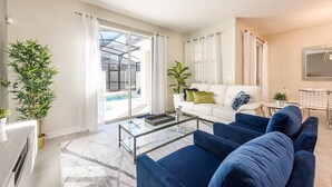 A modern living room with a white sofa, blue armchairs, a glass coffee table, and a large window with curtains. - Last Minute Disney Getaway! Townhouse with Private Pool. Book Now! #21174 (Orlando)
