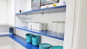 Een keukenkastje met teal- en witte servies, glazen en een koffiezetapparaat.