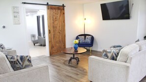 Een woonkamer met een bank, fauteuils, een salontafel en een aan de muur bevestigde televisie.