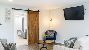 Een moderne woonkamer met twee banken, een salontafel, een aan de muur bevestigde televisie en een houten deur.