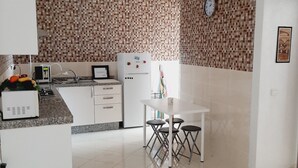 Een moderne keuken met witte kasten, een betegelde achterwand, een eethoek met een witte tafel en stoelen, en een hanglamp.