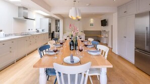 Une cuisine moderne avec une table à manger en bois, disposée pour accueillir six personnes, des chaises blanches et un arrangement floral au centre.