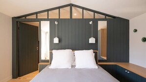 Un dormitorio con una cama, dos almohadas blancas, un banco de madera y una pared oscura con techo inclinado.