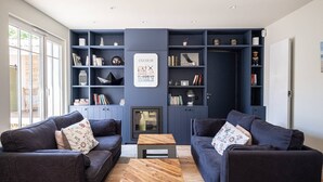 Una sala de estar moderna con estanterías empotradas azul oscuro, dos sofás oscuros, una mesa de centro de madera y una chimenea.