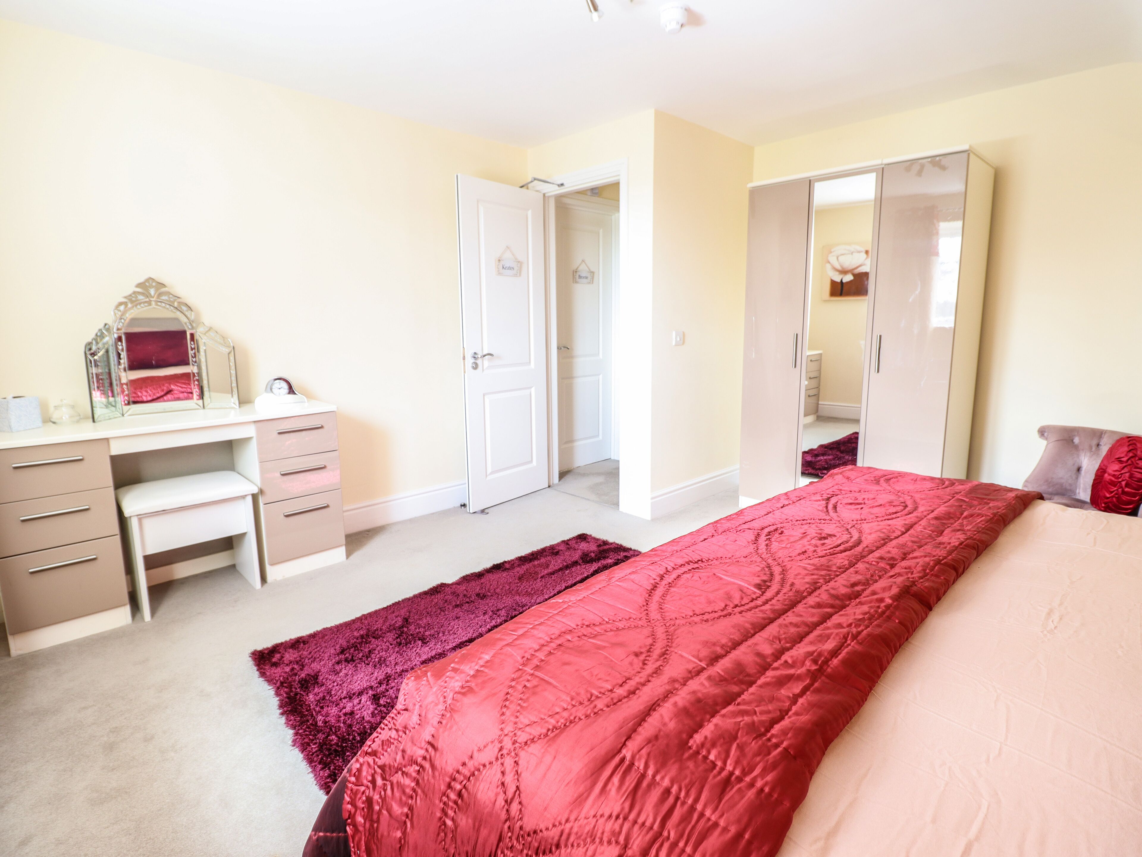 A bedroom with a bed, a desk, a mirror, and a wardrobe.