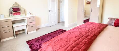 A bedroom with a bed, a desk, a mirror, and a wardrobe.