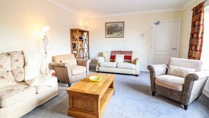A living room with a beige sofa, a wooden coffee table, and a patterned armchair. - Maesbury Manor (Oswestry)