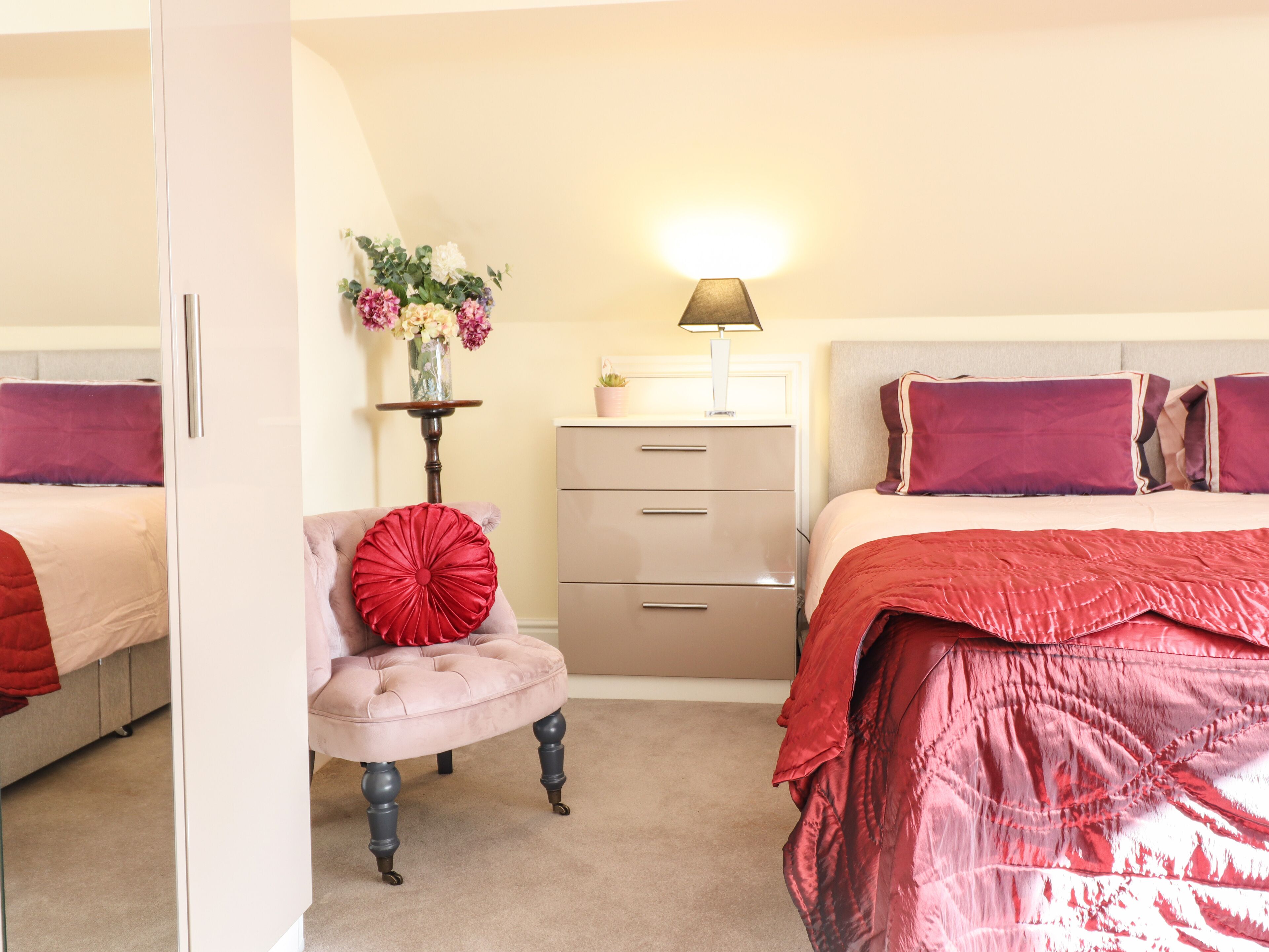 A bedroom with two beds, a dresser, a chair, and a lamp.