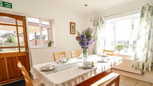 A dining area with a table set for four, chairs, a bench, a vase with flowers, and a fire exit sign. - Maesbury Manor (Oswestry)