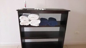 Une étagère en bois foncé, composée de trois étagères, sur laquelle sont pliés des serviettes et posée une bouteille de gel hydroalcoolique.