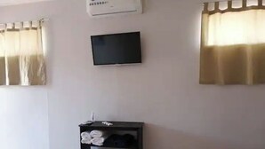 Une chambre dotée d’un téléviseur à écran plat fixé au mur, d’un meuble de rangement noir contenant des serviettes et d’une fenêtre ornée de rideaux beiges.