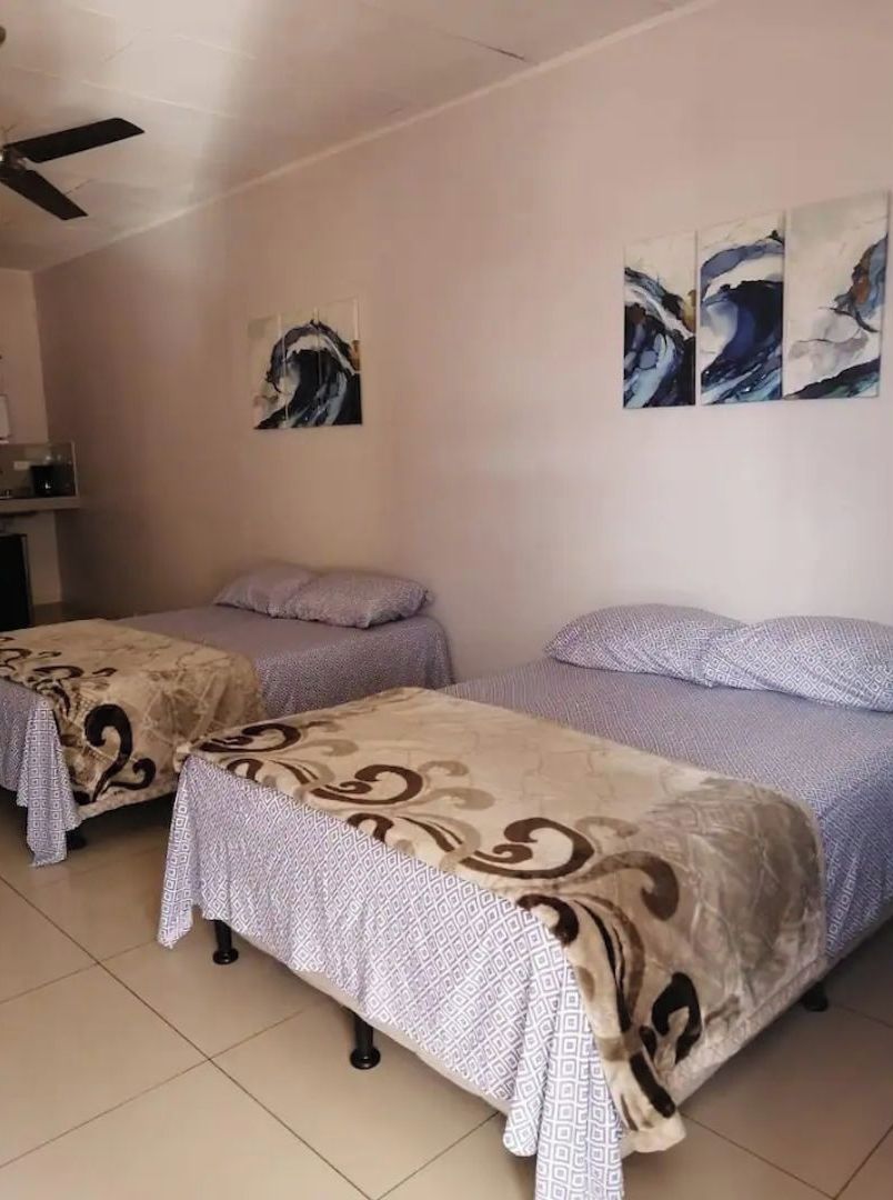 Quarto com duas camas, ventilador de teto e arte abstrata nas paredes.
